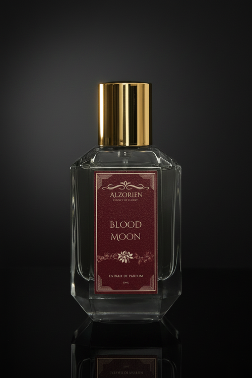 A faceted clear glass perfume bottle with a reflective gold cap and a dark red label reading 'ALZORJEN PARIS' and 'BLOOD MOON', photographed against a dark black background.
